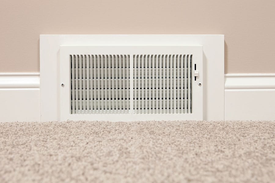 White wall-mounted air vent near a carpeted floor, often checked during furnace repair.